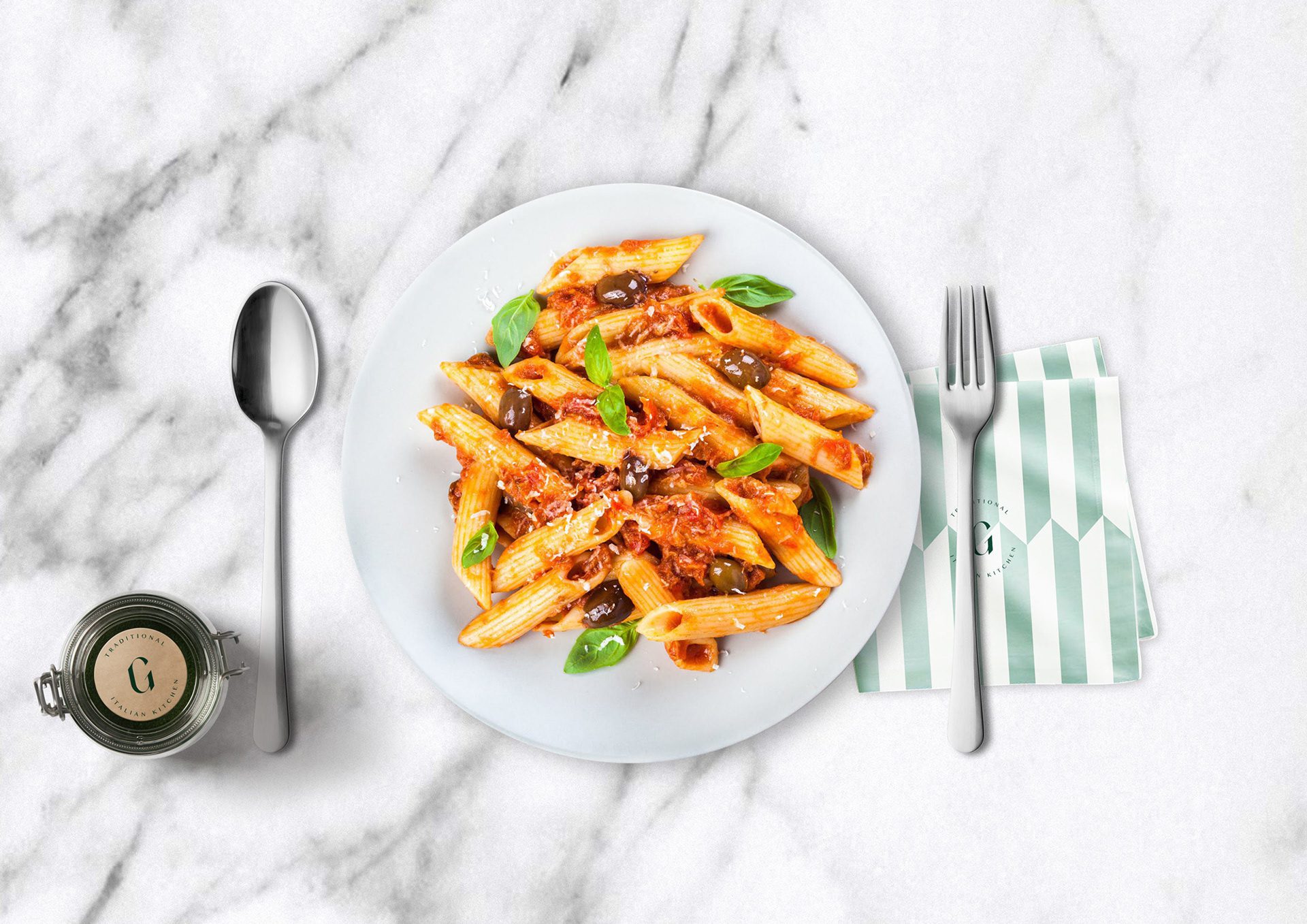 Penne plate on marble with a Gaia jar, cutlery and a striped napkin