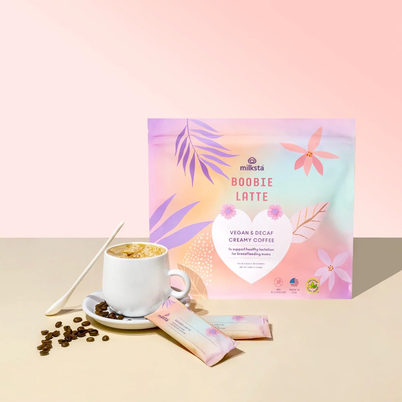 Milksta pouch beside a latte cup, coffee beans and two sachet sticks