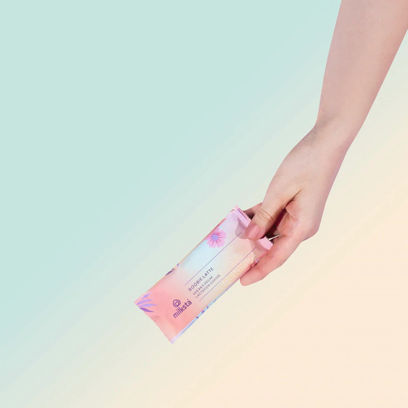 Hand holding a Milksta sachet stick against a mint to peach gradient