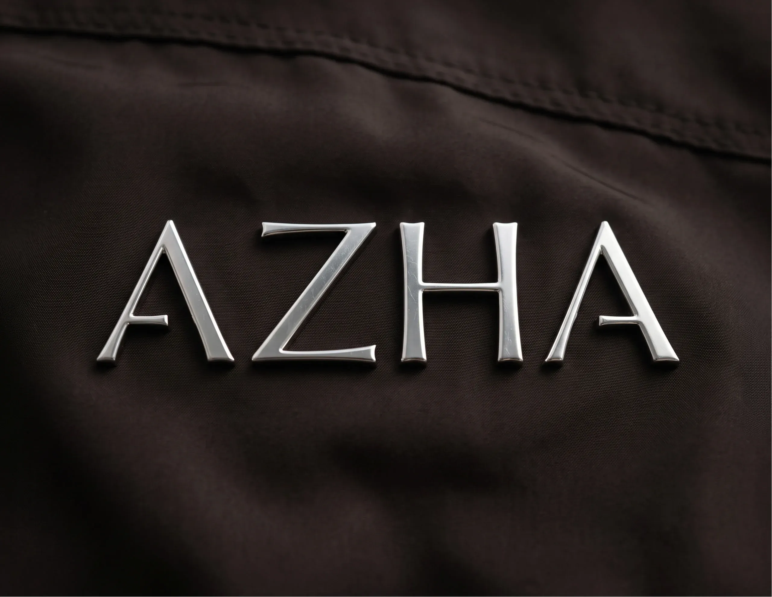 Brushed metal AZHA wordmark on dark fabric